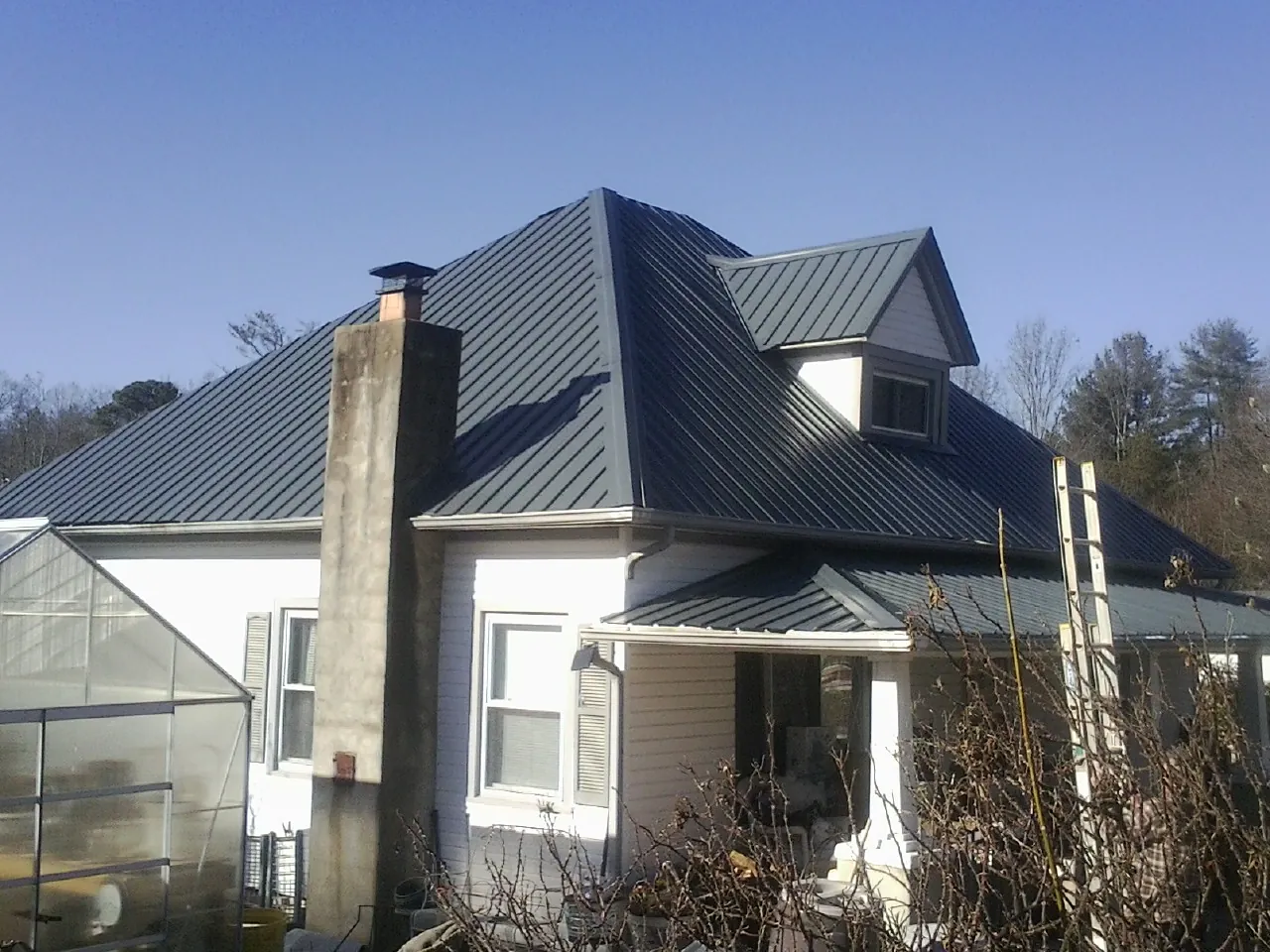Dark blue standing seam metal roof on a white farmhouse with dormer — Slate & Tile Roof Repair by Roofing Brothers in Cedar Knolls