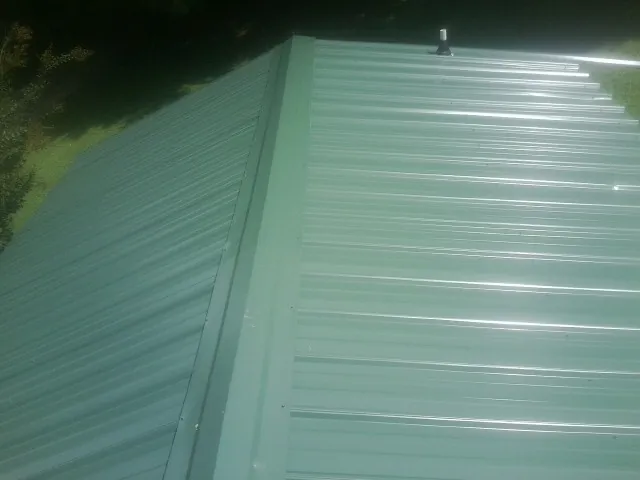 New green metal panels meeting at the ridge of a roof — Flat Roof Repair work by our crew in Cedar Knolls