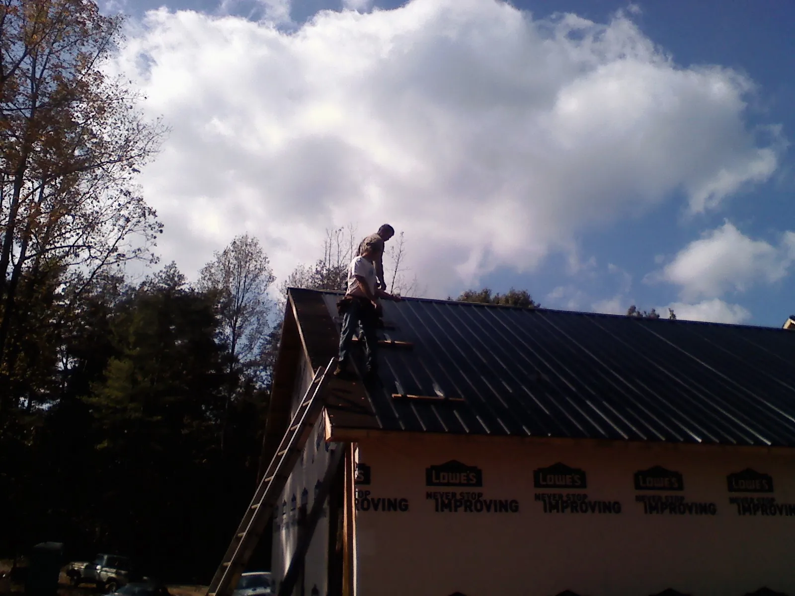 Roofer fastening dark metal panels high against a cloudy sky, from a Roof Inspection job in Cedar Knolls