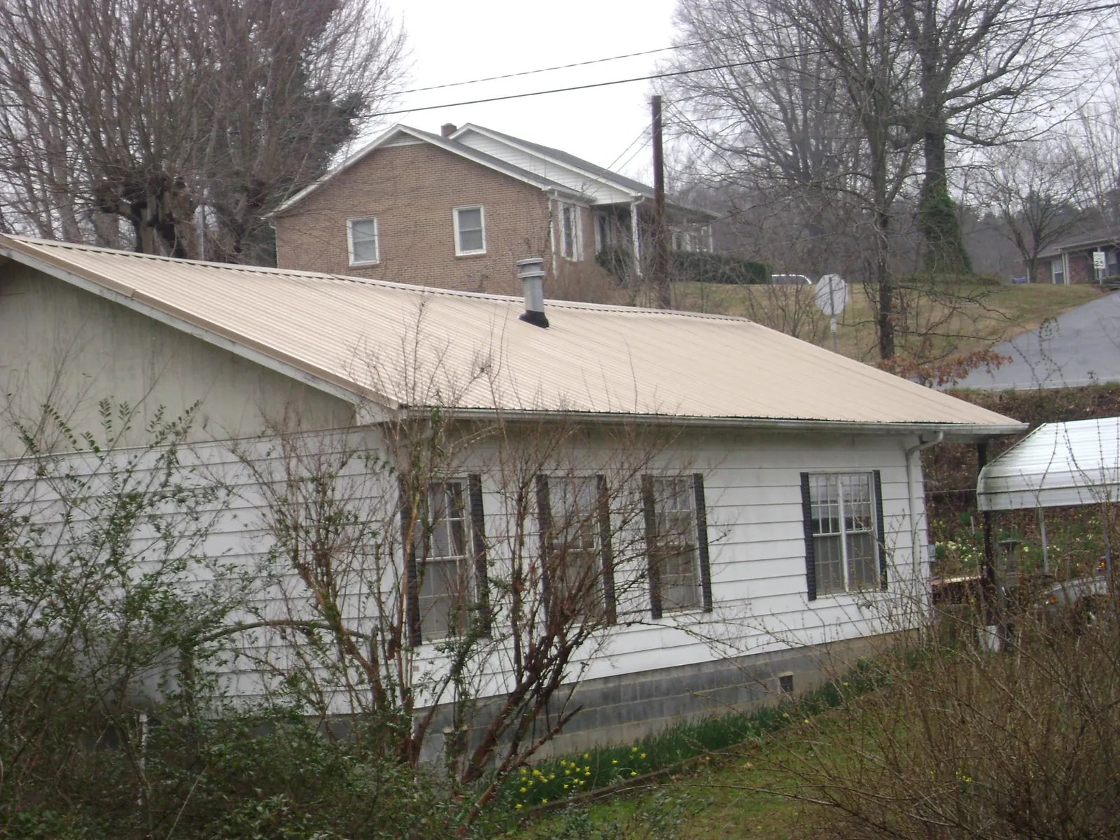 Tan metal roof on a white sided house set into a hillside — Commercial Roofing by Roofing Brothers in Cedar Knolls